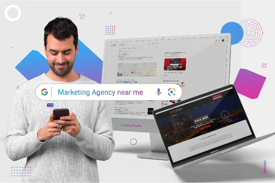 A man is looking at his phone while holding a laptop.